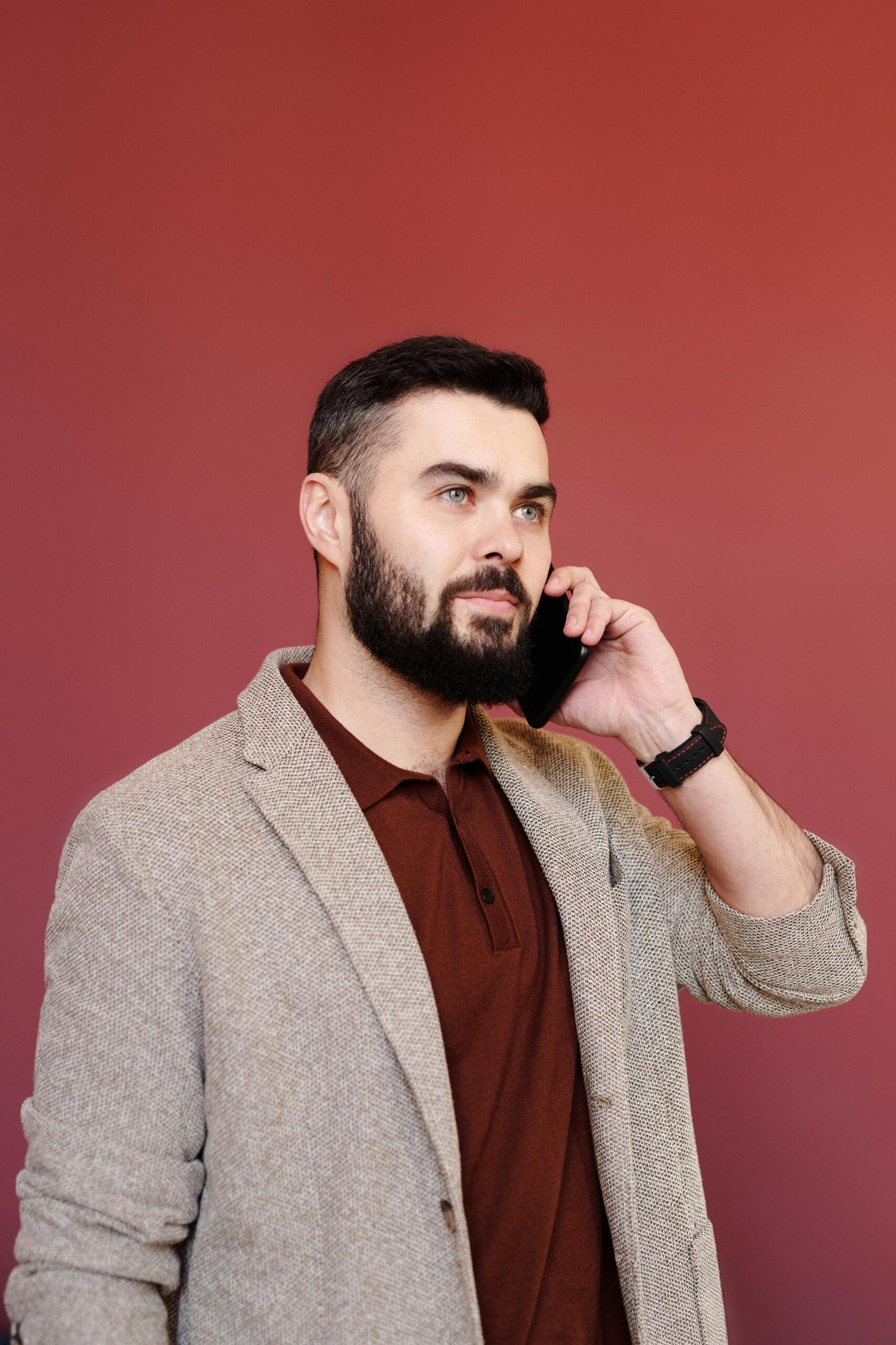 Professional man in a brown coat using smartphone against red background.